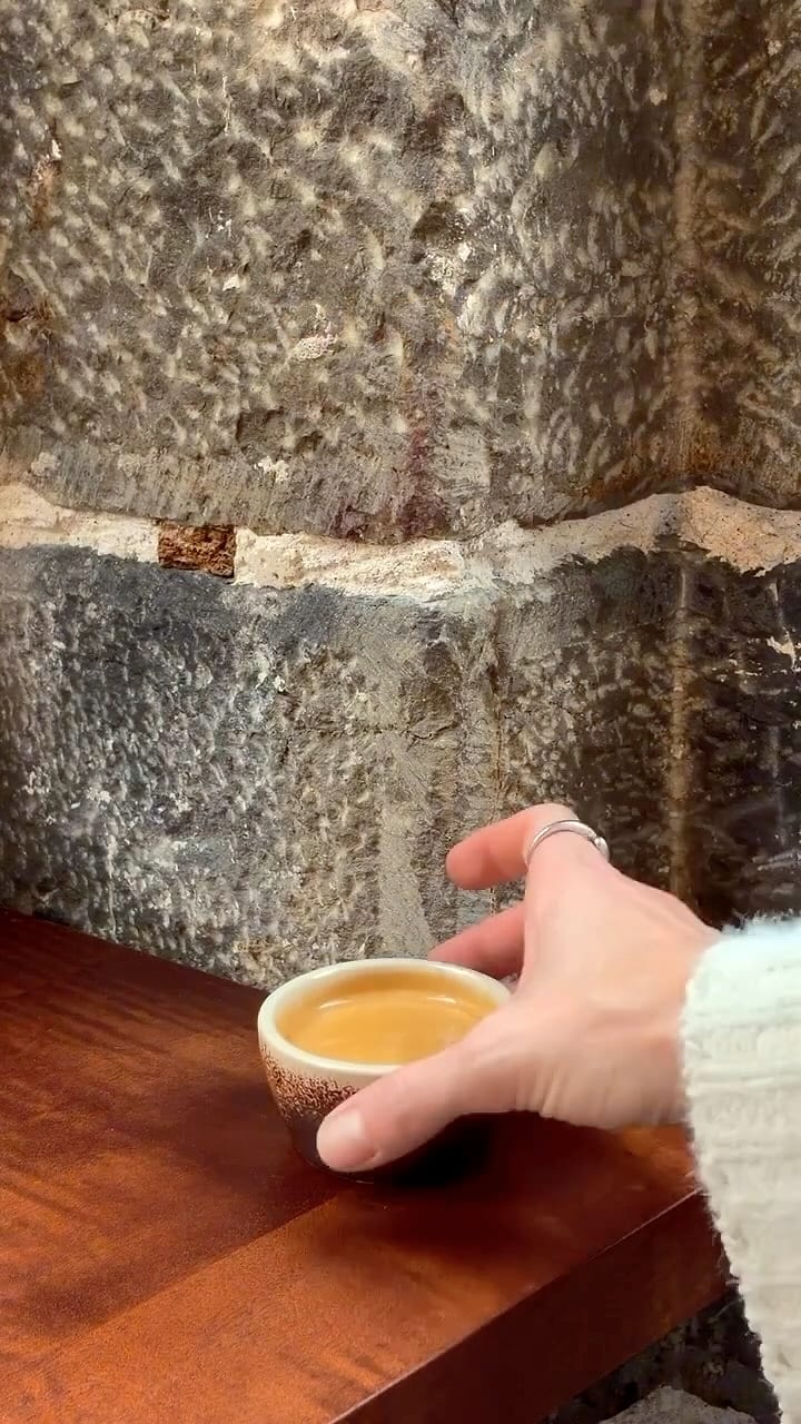 Un cappuccino au motif dessiné, un verre d'eau et un carré de granola sur un plateau en inox.