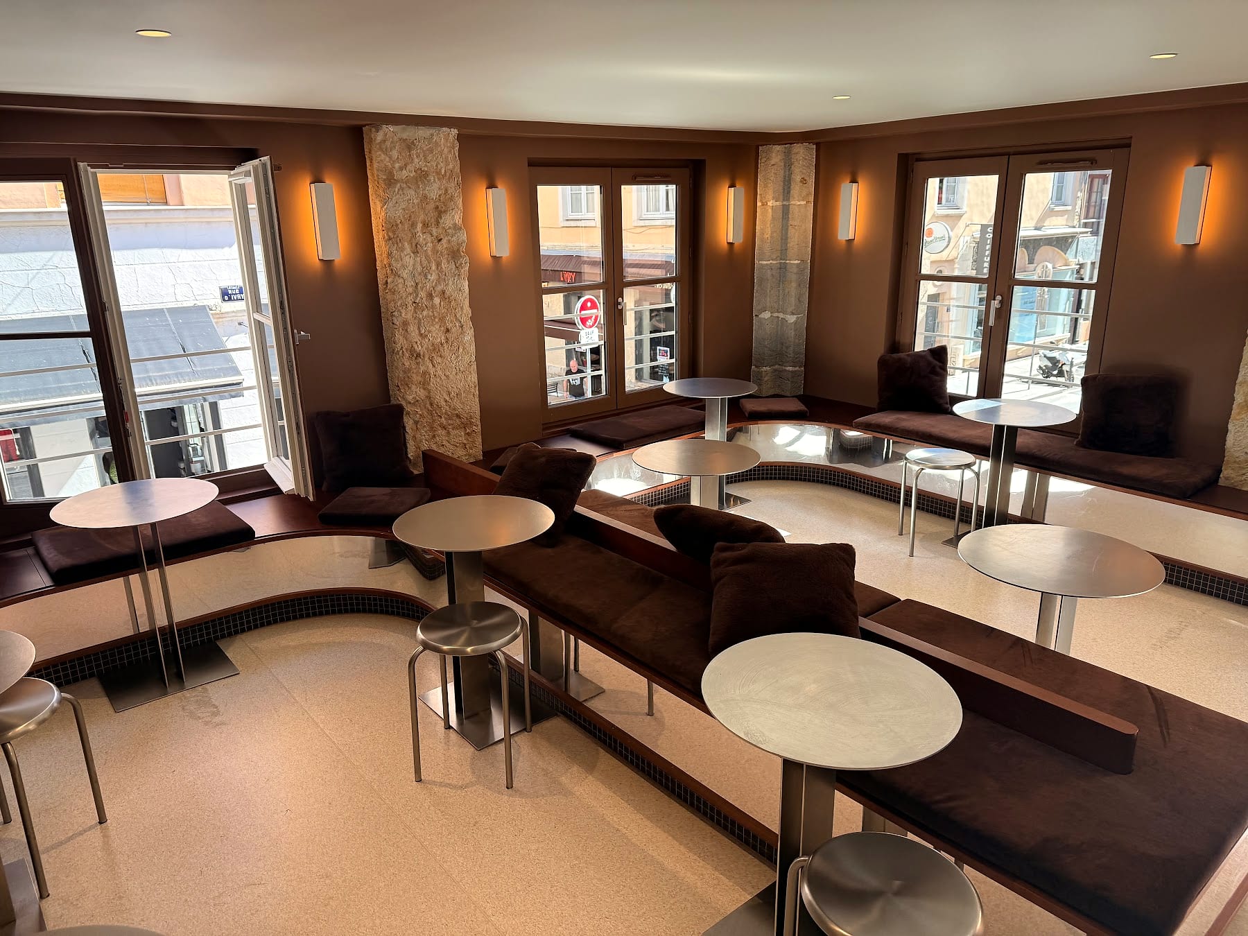 L'étage, les banquettes de velours brun et les tables rondes dans la lumière des fenêtres d'angle.