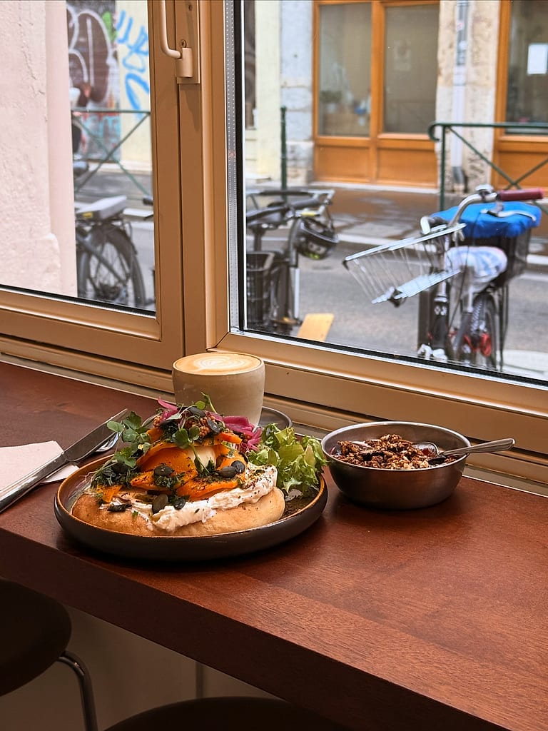 Une tartine garnie et un cappuccino sur le comptoir de bois, devant la baie vitrée.