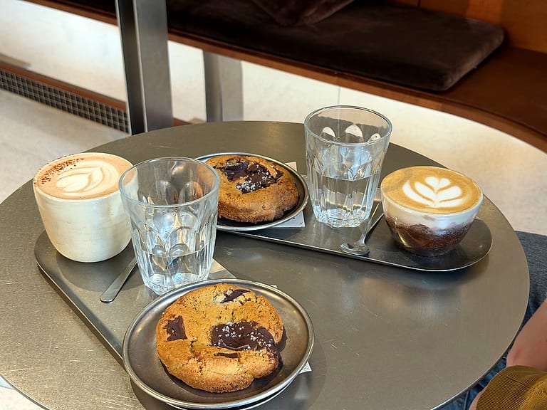 Deux cappuccinos et deux cookies sur un plateau en inox, posé sur une table de l'étage.