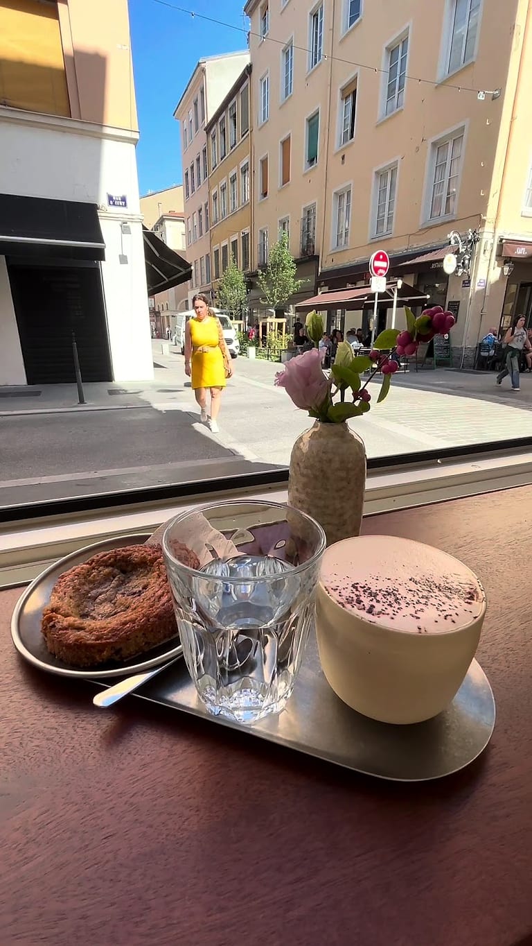 Un cookie et un cappuccino posés devant la fenêtre, la rue du Mail derrière la vitre.